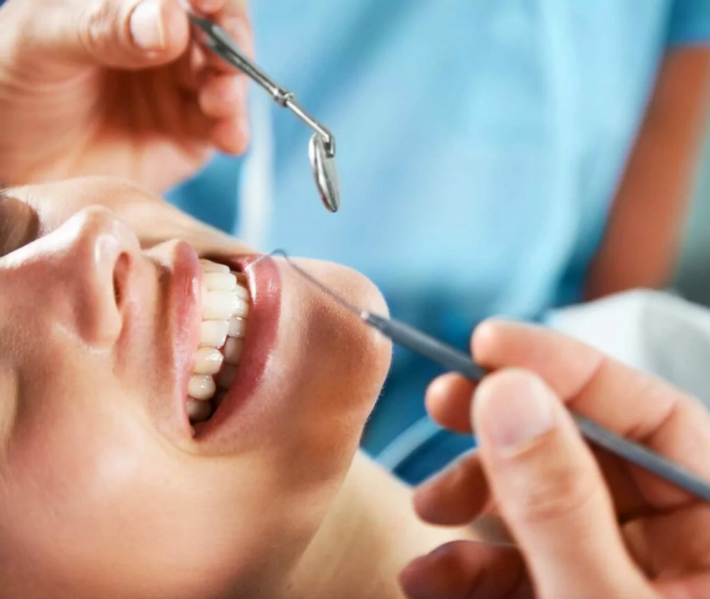 A close-up of a dental examination with a patient lying back and a dentist or dental hygienist using dental tools to inspect the patient's teeth.