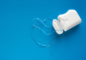 A white dental floss container with the lid open reveals the floss inside, partially pulled across a blue surface. The clean design emphasizes personal oral hygiene, showcasing a common tool for interdental cleaning.