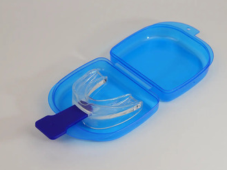 Transparent dental mouthguard with blue handle placed inside open blue plastic storage case with hinged lid.